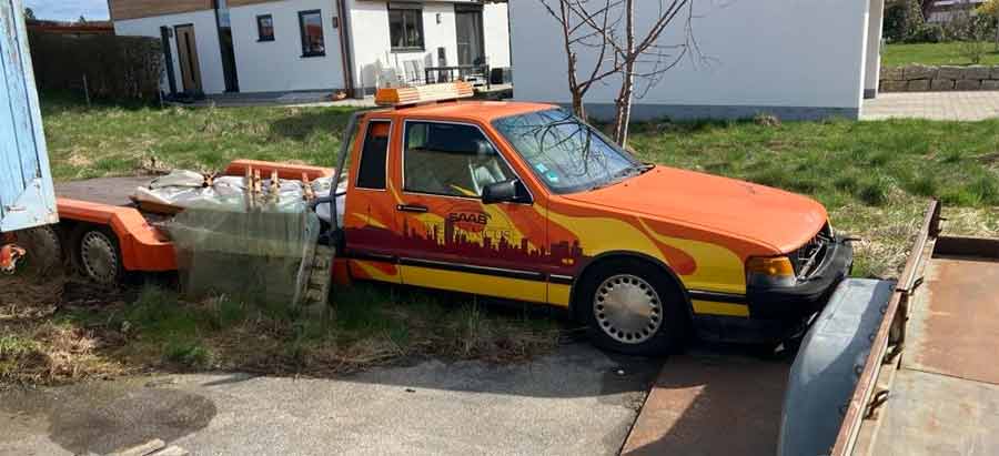 Once a proud carrier of automotive dreams, the Saab 9000 Auto Transporter now rests, abandoned and embraced by nature, its vibrant colors fading into the surrounding greenery.