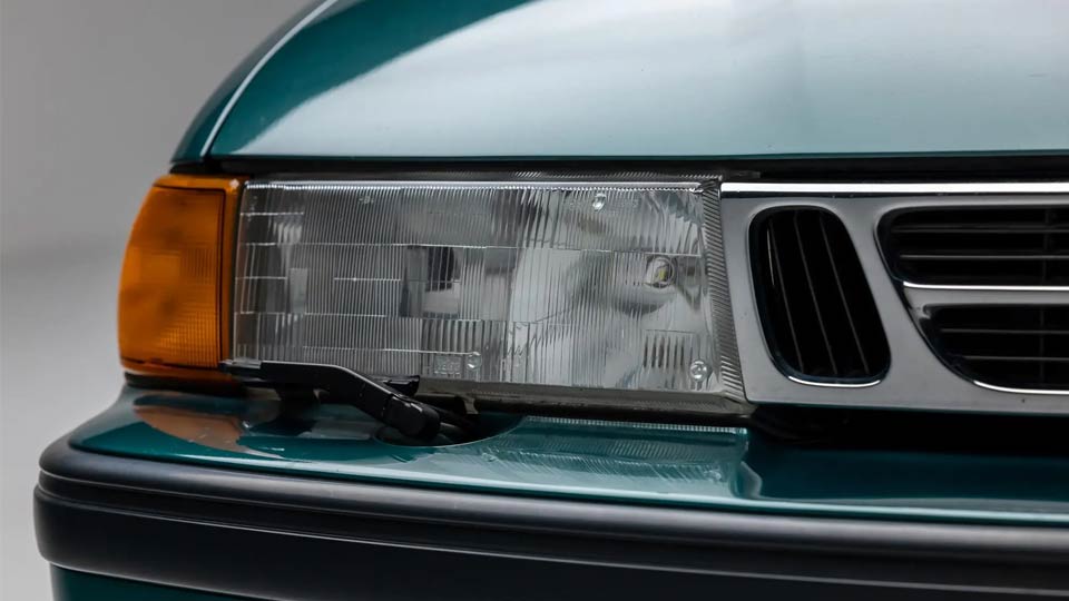 Despite nearly three decades since it first hit the road, the headlight assembly of this 1994 Saab 9000 Aero remains in near-showroom condition. The original glass, surrounded by pristine Eucalyptus Green paint, exemplifies the car's meticulous care and preservation, a true testament to its low mileage and careful ownership.