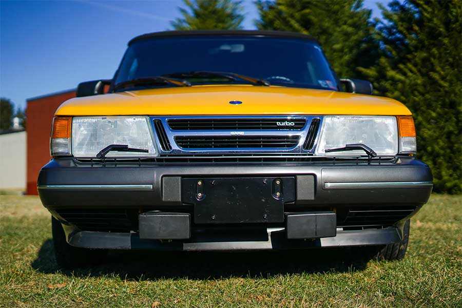 A close-up of the 1991 Saab 900 Turbo’s front fascia, emphasizing its iconic headlight wipers, signature grille, and legendary Monte Carlo Yellow finish.