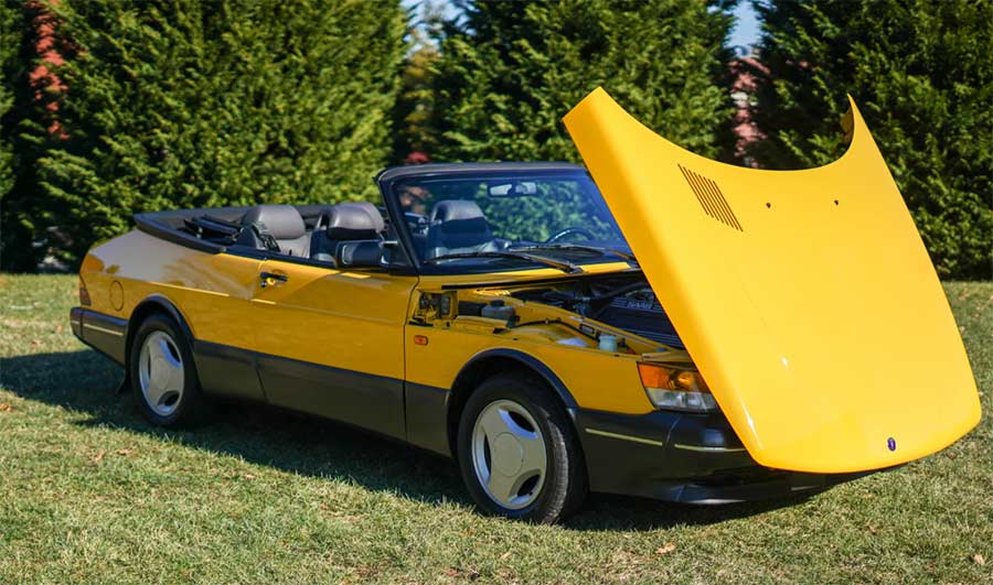 A vibrant Monte Carlo Yellow 1991 Saab 900 Turbo Convertible with its front-hinged hood raised, revealing the robust turbocharged 2.0-liter inline-four.