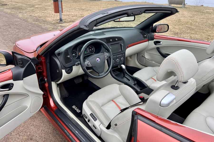 The luxurious interior of the Saab 9-3 Aero Cabriolet Independence Edition, featuring premium leather seats with orange stitching and a Hirsch carbon fiber-wrapped instrument panel.