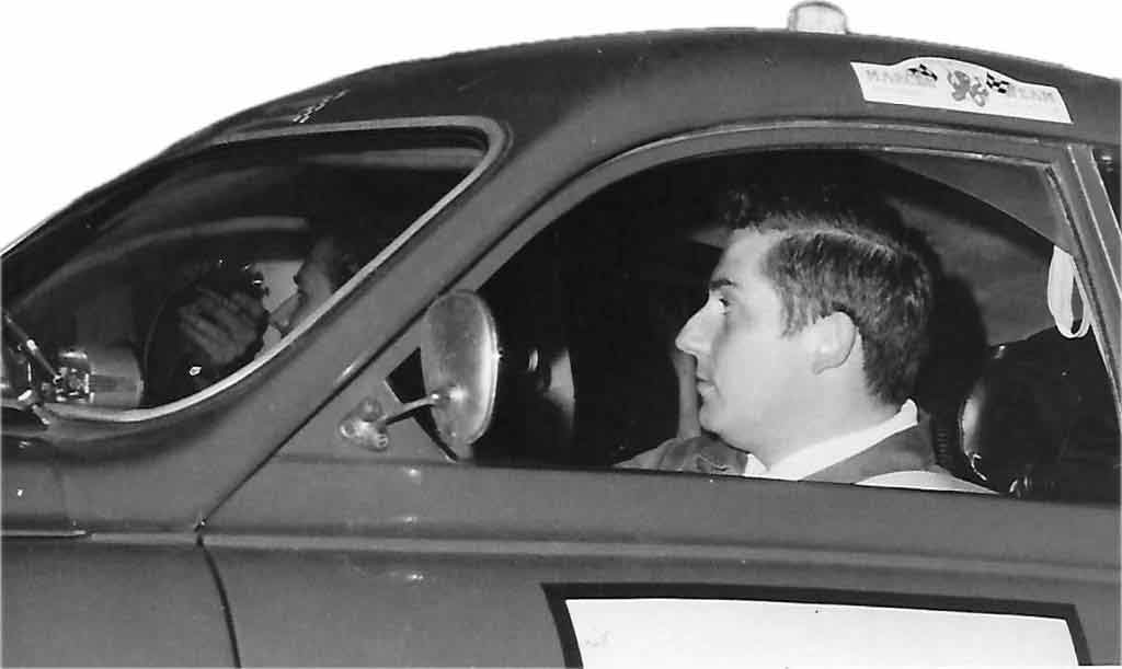 Captured in time: A young Hans Wagemans behind the wheel of his favorite Saab 96, in a classic black and white photograph. This moment frozen in time showcases a youthful Hans, filled with enthusiasm and ambition, as he navigates the road ahead. The Saab 96, an icon of design and engineering, serves as the perfect companion for his adventurous spirit. This image is a testament to the beginnings of a lifelong journey of passion for automotive excellence.