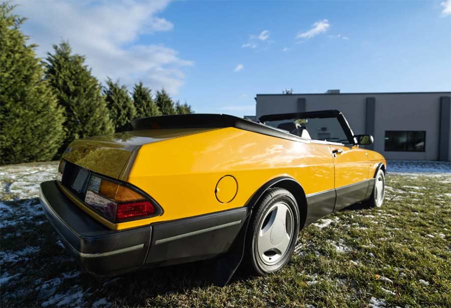 A pristine rear-quarter view of the 1991 Saab 900 Monte Carlo Yellow convertible, showcasing its bold stance and timeless body lines.