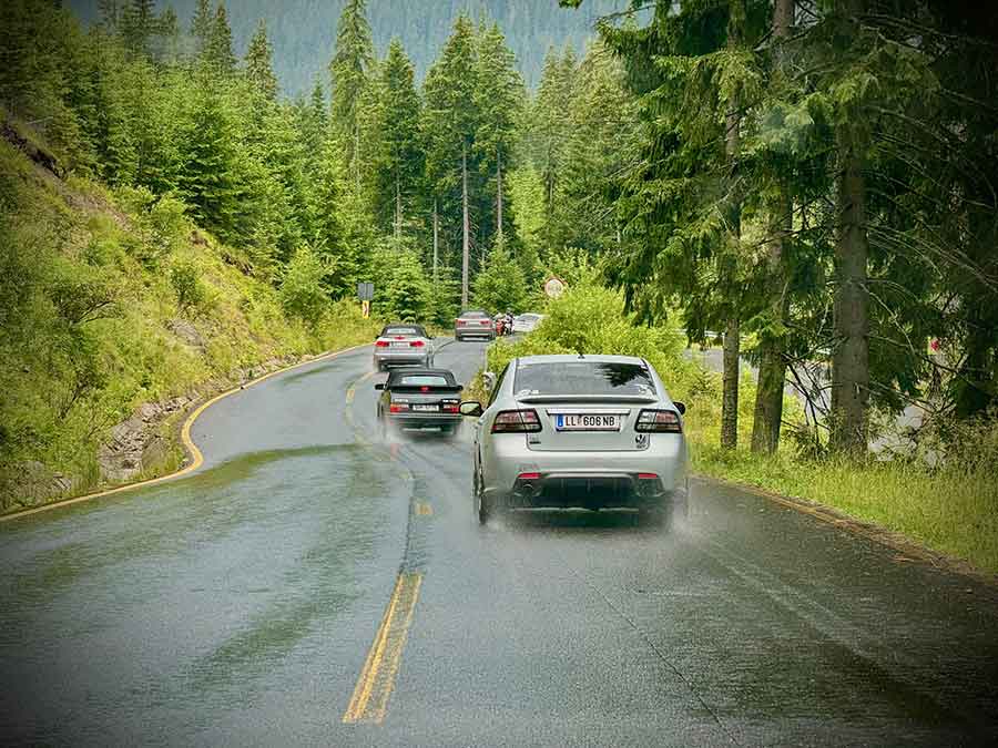 A convoy of Saab cars drives through the lush and scenic roads of Transylvania, highlighting the thrill and beauty of the journey.