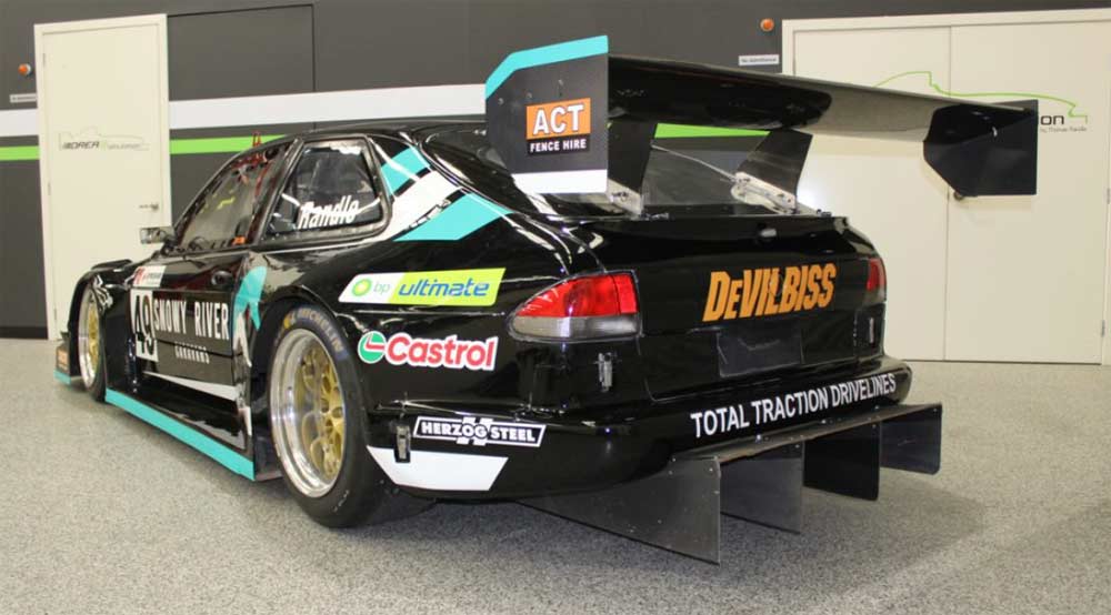 Rear view of Thomas Randle's 750-plus horsepower Saab 9-3, showcasing its impressive aerodynamic features and sponsor decals, ready for the Precision National Sports Sedan series at The Bend Motorsport Park.