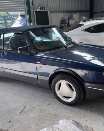 The Saab 900 Convertible in its resting glory, revealing a blue hue that mirrors the sky above. This project car, enveloped by the quietude of a storage facility, promises the road's embrace with a little tender care and mechanical craftsmanship.