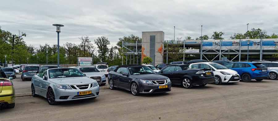 Saab convertibles proudly stand out among other vehicles in a parking lot, ready to start another leg of their journey during the 2024 Saab Convertible Weekend, highlighting the distinctive appeal of these classic cars. (photo by David Joost Kamermans)