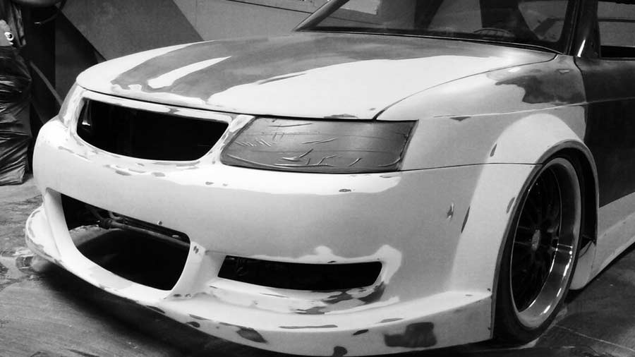 A close-up of the Saab 900 2.0T WideSide Edition during its bodywork phase, capturing the meticulous shaping and customization of the front bumper and wide fenders, a key part of its unique transformation.