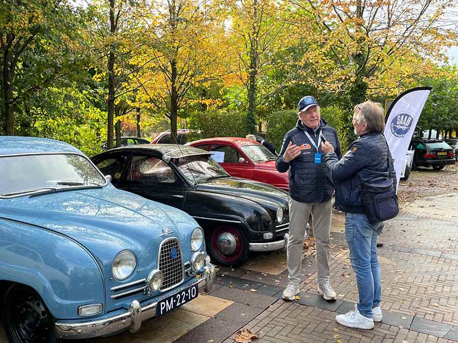 Saab enthusiasts deep in conversation at the event, surrounded by classic Saab 92s and 96s.