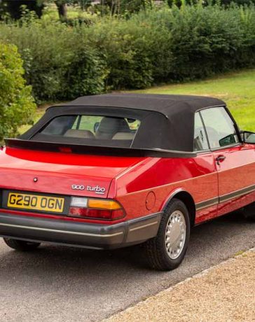 the iconic 1990 Saab 900 Turbo 16 Convertible in vibrant red, a classic symbol of sophistication and performance, as it stands gracefully in a lush setting.