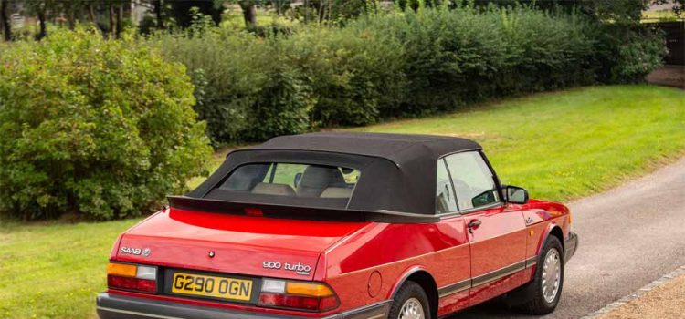 the iconic 1990 Saab 900 Turbo 16 Convertible in vibrant red, a classic symbol of sophistication and performance, as it stands gracefully in a lush setting.