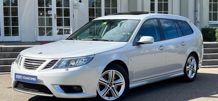 An exquisite Snow Silver Saab 9-3 SportEstate Turbo X with a panoramic sunroof parked outside a modern building, highlighting its sleek design and advanced engineering for the discerning collector.