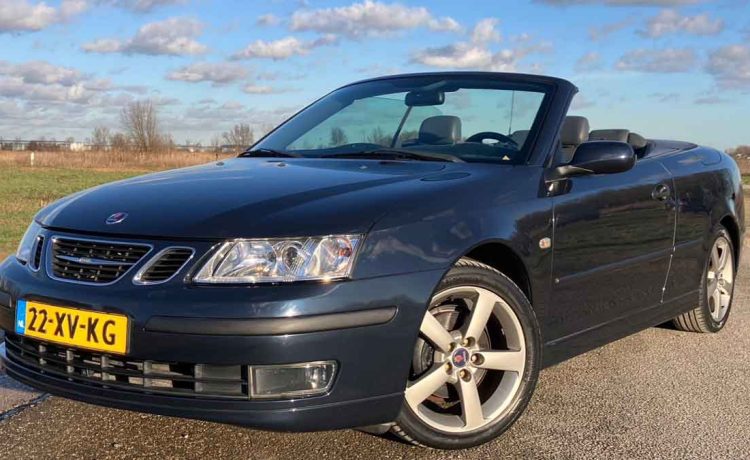 A sleek blue Saab 9-3 Vector Cabriolet with the top down, showcasing its sporty alloy wheels and two-tone leather interior, parked under a clear sky.