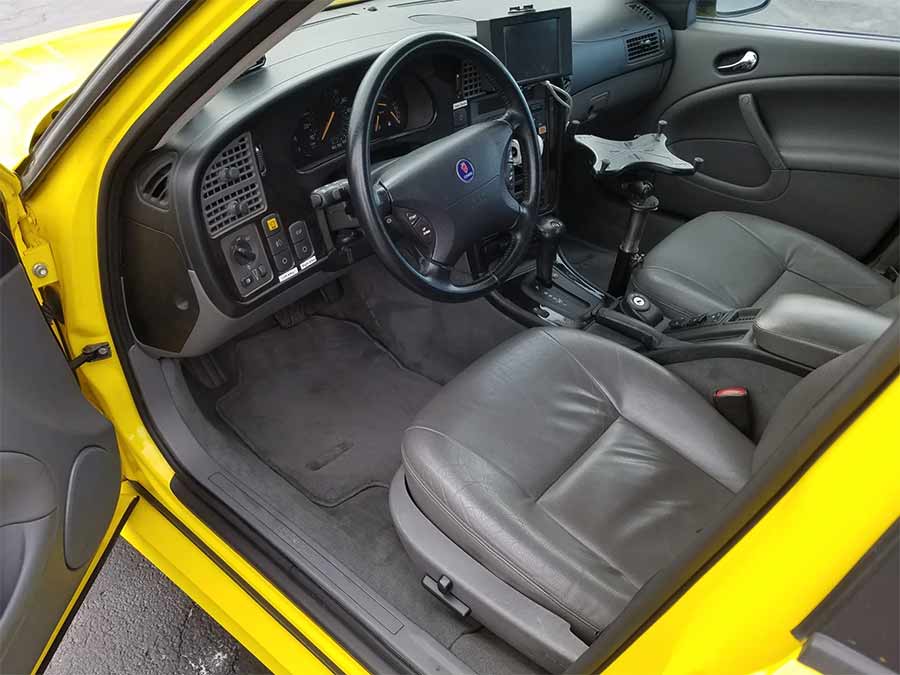 The interior of the 2004 Saab 9-5 Arc Friction Tester, showcasing its retrofitted control panel for runway friction testing, alongside the premium heated leather seats and classic Saab dashboard design.