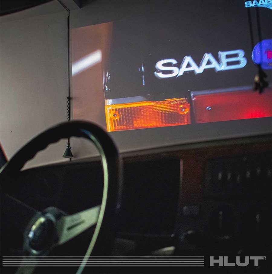 Captivating scene at the Saab exhibition with a Saab 900 on display and vintage Saab promotional films projected on the gallery wall.