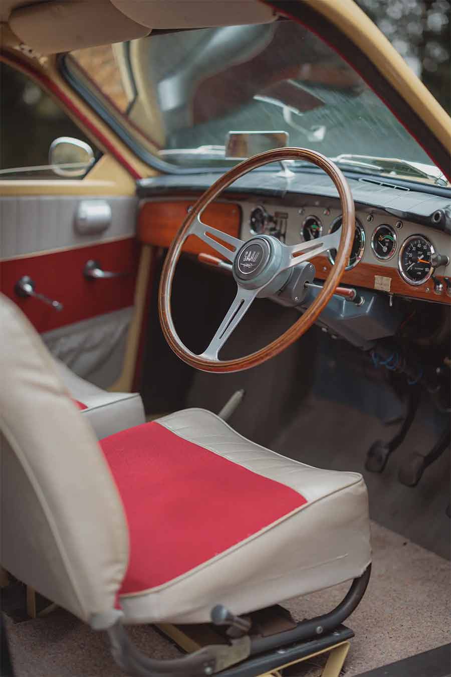 The fully restored interior of the 1966 Saab 96 showcases a perfect blend of Swedish simplicity and craftsmanship, featuring a wood-rimmed steering wheel, column-mounted gear lever, and period-correct fabric upholstery.