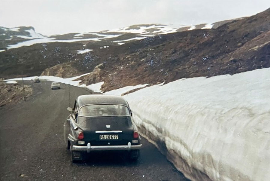 A midnight-blue Saab 96 gliding through the snowy Norwegian roads in 1966, showcasing both scenery and the car’s confident two-stroke spirit.