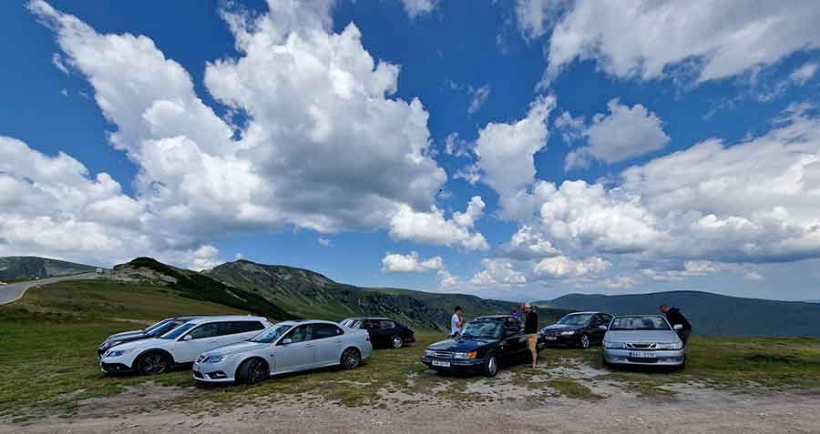 Saab enthusiasts gather at a breathtaking mountain viewpoint during their Transylvania tour, showcasing a variety of Saab models against the stunning backdrop.