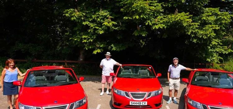 Uniting through their shared passion, Jane Hughes, Vincent O'Brien, and Charles Richards proudly pose with their rare red Saab convertibles, showcasing the timeless elegance of these remarkable vehicles against the backdrop of Formby's picturesque streets. Their chance meeting and love for these classic cars have created an unbreakable bond that continues to flourish in the heart of their tight-knit community.