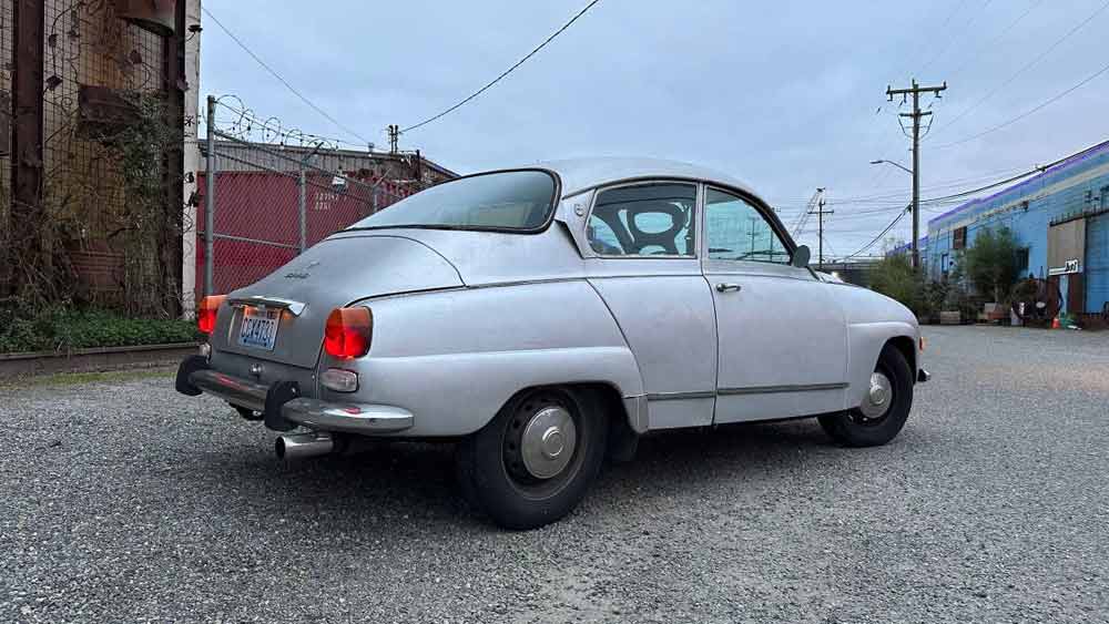 Classic Saab 96 V4 in Silver: A Snapshot of Automotive Heritage on an Industrial Backdrop.