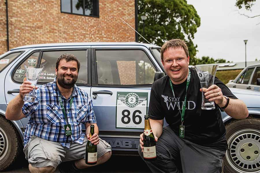 Victory is sweet! Alistair Leckie and Matt Outhwaite celebrate their first win after 18 months of rallying, proudly holding the trophy with their trusty SAAB 900 Turbo in the background. 