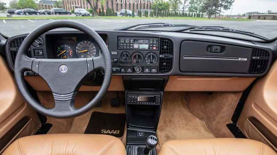 The timeless interior of the SAAB 900 Turbo 16 S, featuring a driver-focused dashboard with iconic aircraft-inspired controls. The combination of tan leather seats and ergonomic design showcases SAAB's commitment to comfort and functionality, making it a classic in both style and performance. Photo credit: Automotive Fever.