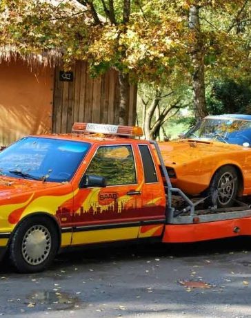 In its prime, a Saab 9000 Auto Transporter in a striking livery confidently carries a bright orange Saab Sonett II sports car. A snapshot of Saab's ingenuity and versatility, epitomizing the golden era of Saab's automotive excellence