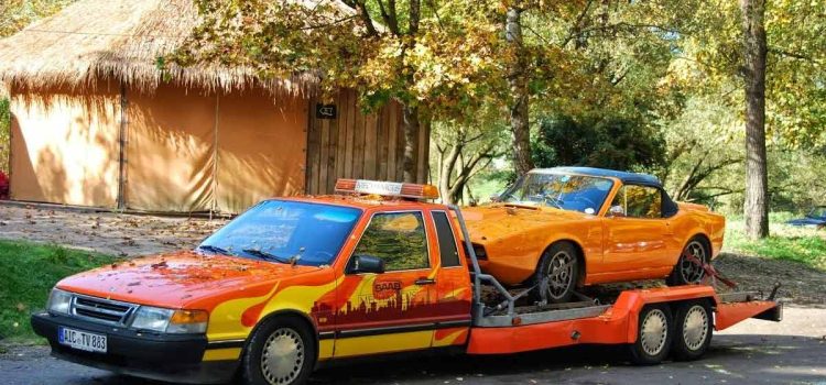 In its prime, a Saab 9000 Auto Transporter in a striking livery confidently carries a bright orange Saab Sonett II sports car. A snapshot of Saab's ingenuity and versatility, epitomizing the golden era of Saab's automotive excellence