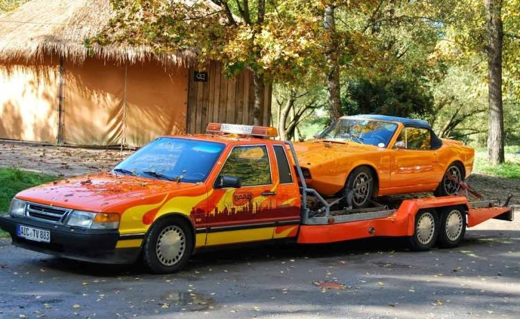 In its prime, a Saab 9000 Auto Transporter in a striking livery confidently carries a bright orange Saab Sonett II sports car. A snapshot of Saab's ingenuity and versatility, epitomizing the golden era of Saab's automotive excellence