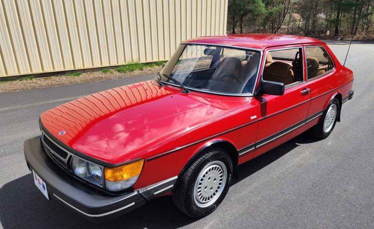 A pristine 1985 SAAB 900S Coupe in its classic cherry red paint, perfectly preserved and reflecting its era's design with sleek lines and distinctive round headlights, stands as a testament to automotive history and timeless appeal.