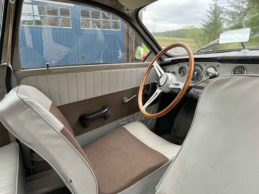 The well-preserved interior of the 1964 Saab 96, showcasing the original two-tone seats and distinctive wooden steering wheel, reflecting its authentic mid-century character.