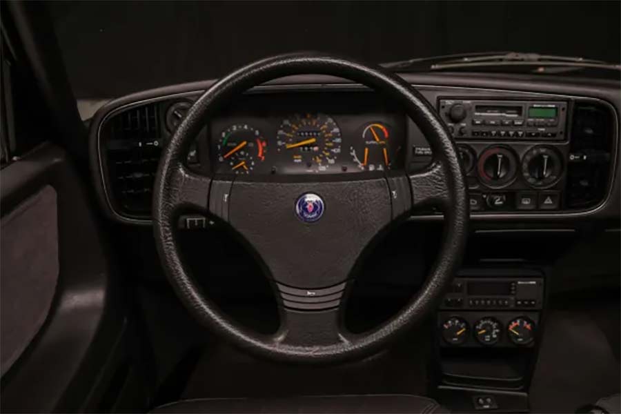 The driver's cockpit of the 1988 Saab 900 Turbo SPG features the iconic Saab padded steering wheel, VDO instrumentation, and the classic Saab/Clarion AM/FM/cassette stereo, creating a familiar and nostalgic experience for all Saab drivers.