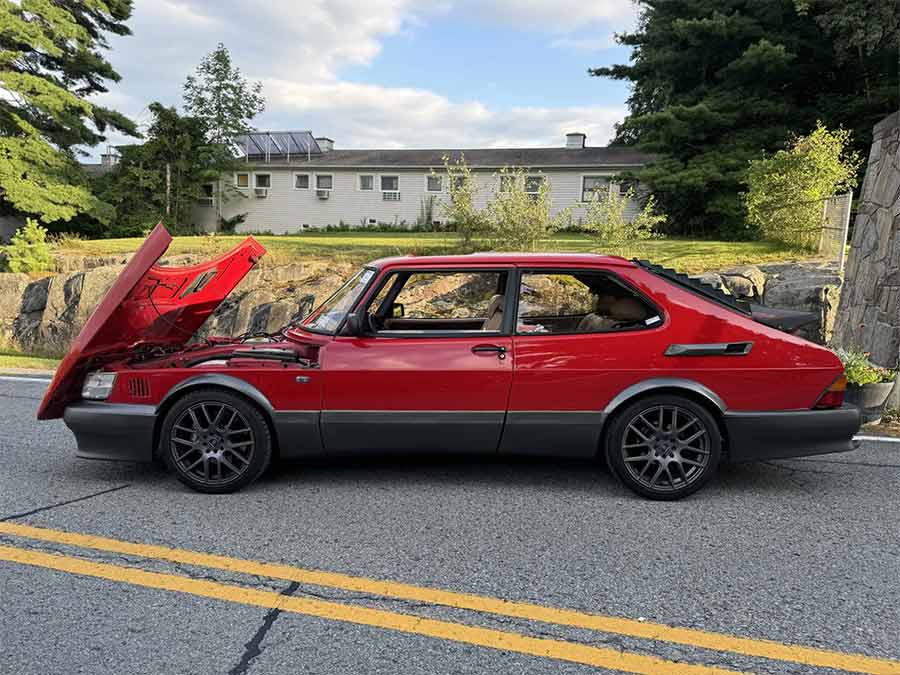 Profile view of the 1990 Saab 900 Turbo SPG, showcasing its Talladega Red finish, aggressive stance with aftermarket 17” wheels, and the modified turbocharged engine ready for performance.