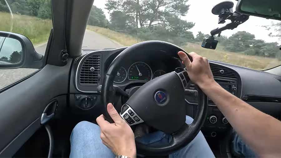 A thrilling moment behind the wheel of a Saab 9-3 Turbo X, captured from the driver's perspective. The image showcases the distinct Saab cockpit design, featuring the iconic three-spoke steering wheel and driver-focused dashboard, reinforcing Saab’s dedication to an engaging driving experience.