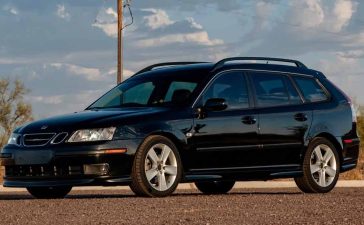 a well-maintained black 2006 Saab 9-3 Aero SportCombi parked outdoors. The car has a sleek design, featuring five-spoke alloy wheels, roof rails, and a sunroof. The front of the car is distinct with its Xenon headlights and fog lights.