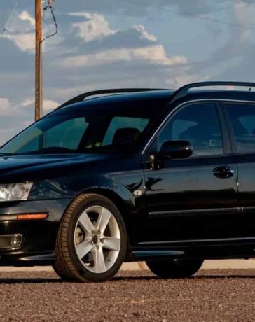 a well-maintained black 2006 Saab 9-3 Aero SportCombi parked outdoors. The car has a sleek design, featuring five-spoke alloy wheels, roof rails, and a sunroof. The front of the car is distinct with its Xenon headlights and fog lights.