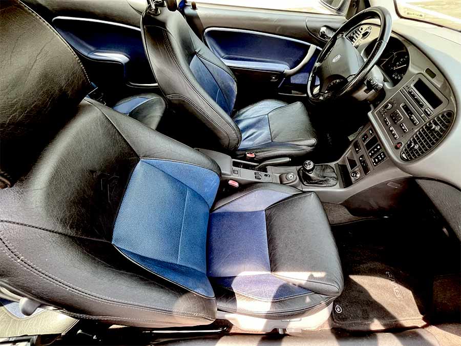  the 1999 Saab 9-3 Viggen, featuring Rocky Black and Deep Blue leather upholstery. The heated, power-adjustable front seats provide comfort and style, while the cabin includes modern amenities such as a cassette stereo, cruise control, automatic climate control, and Viggen-branded door sill plates. The dashboard is well-equipped with a variety of controls and displays, emphasizing both functionality and a driver-centric design.